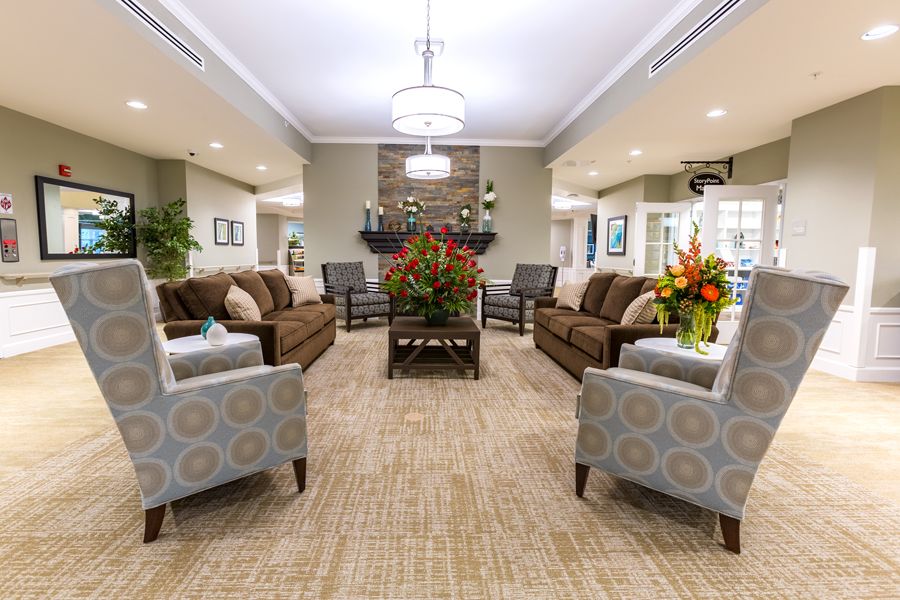 A cozy living room with sofas and chairs arranged around a fireplace, featuring a centrally placed coffee table adorned with flowers.