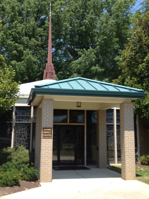 A small church building with a steeple and trees surrounding it.