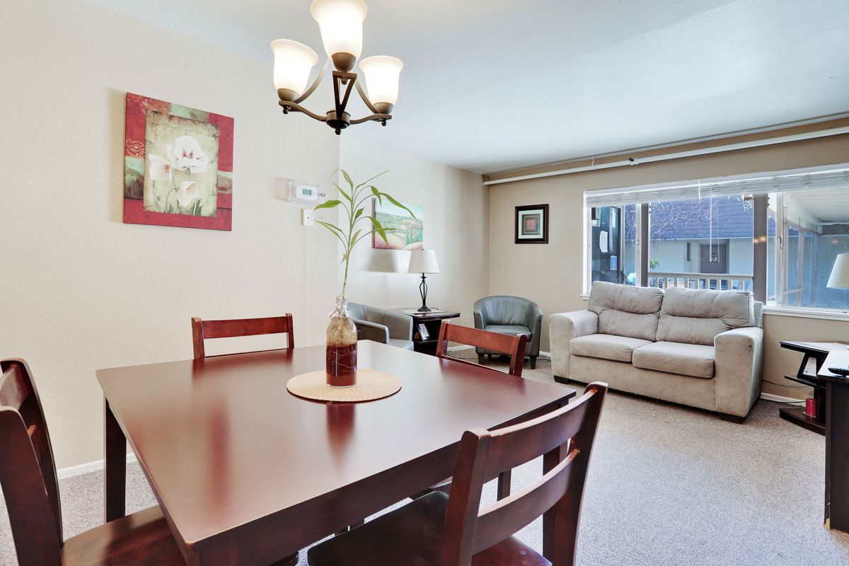 A cozy dining and living area with a wooden table, chairs, and a sofa under natural lighting.