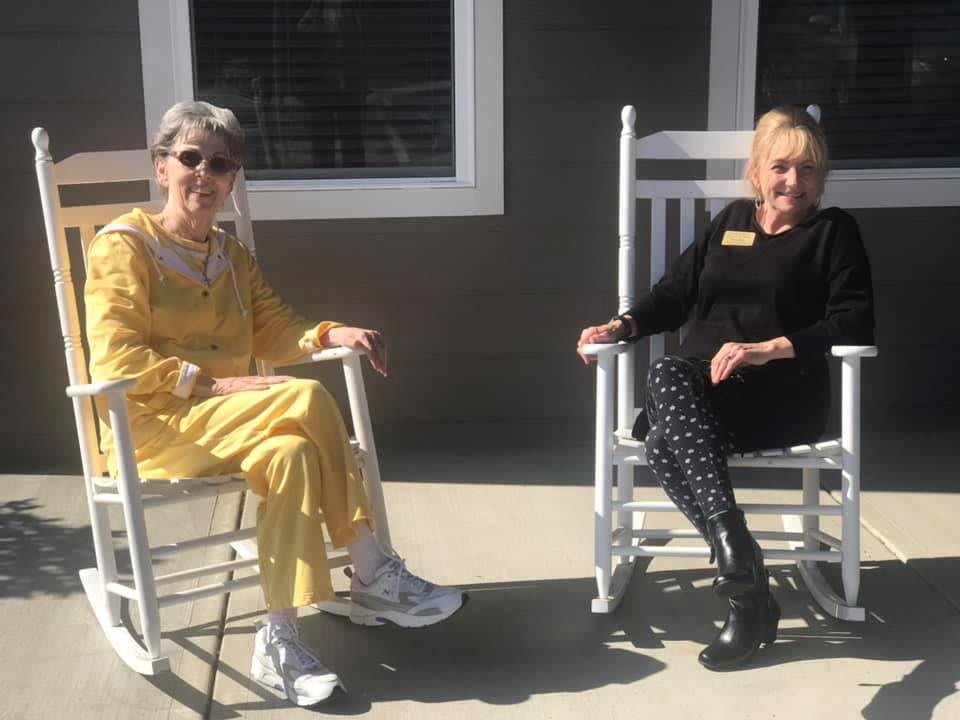 Two people sitting in rocking chairs outside on a sunny day.