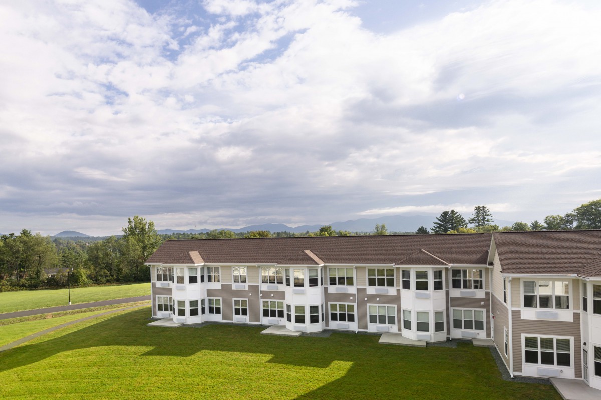 A row of residential apartments with a large green lawn under a cloudy sky.
