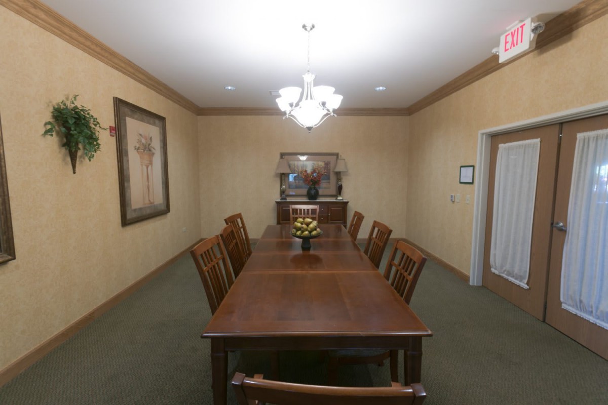 A formal dining room with a long wooden table, surrounded by chairs and lit by a chandelier.