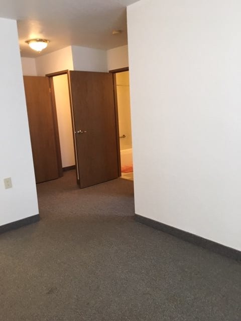 An empty room with a carpeted floor and open doorways leading to other areas.
