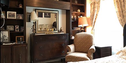 A cozy living room corner featuring an armchair, a dark wooden dresser with a mirror, and warm lighting from table lamps.