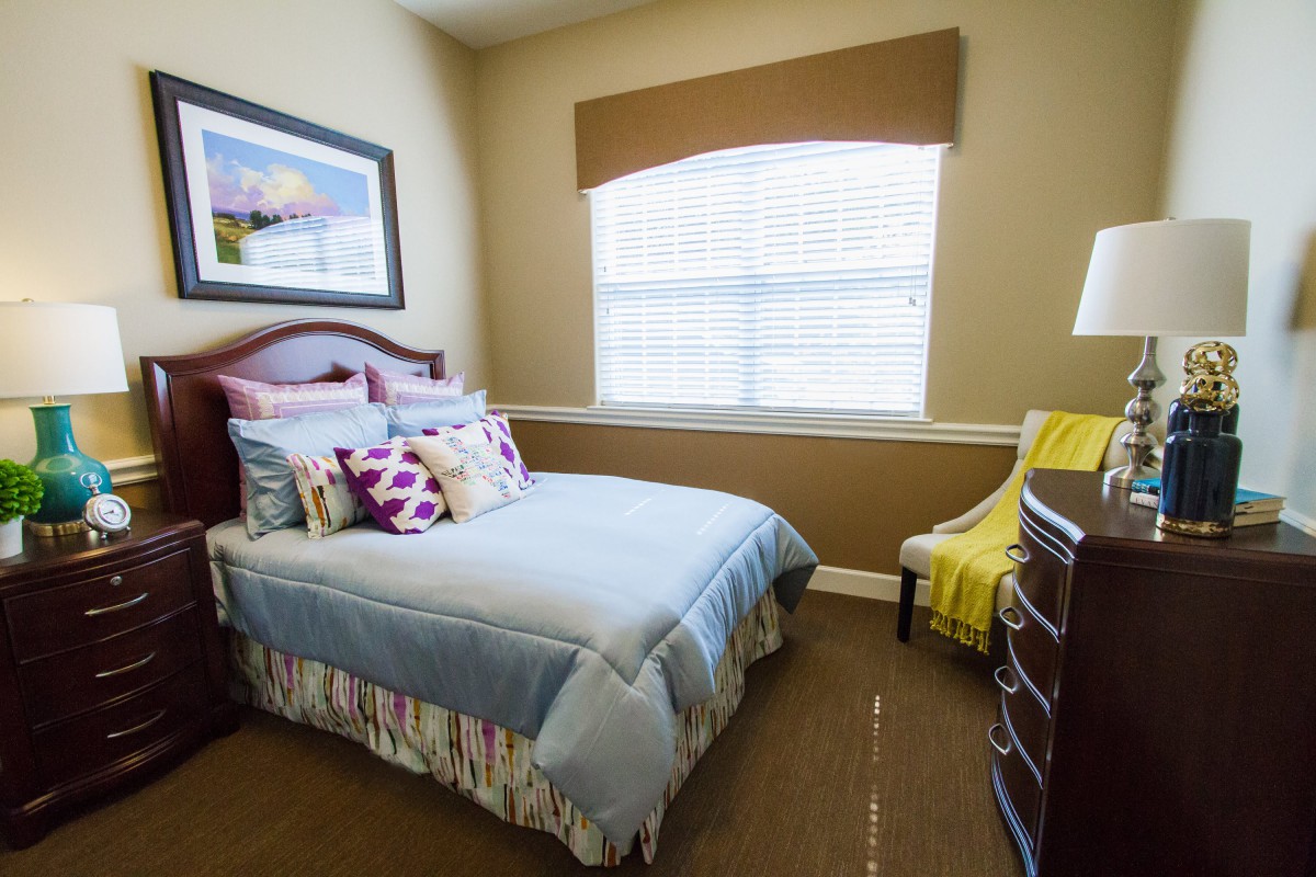 A cozy bedroom with a neatly made bed, decorative pillows, and a large window letting in natural light.
