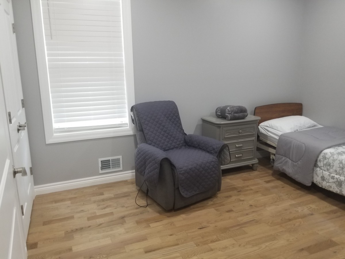 A minimalist bedroom with a gray armchair, bed, and nightstand on a wooden floor.