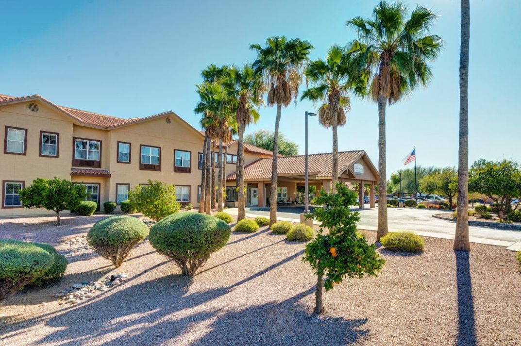 A sunny day view of a hotel surrounded by palm trees and desert landscaping.