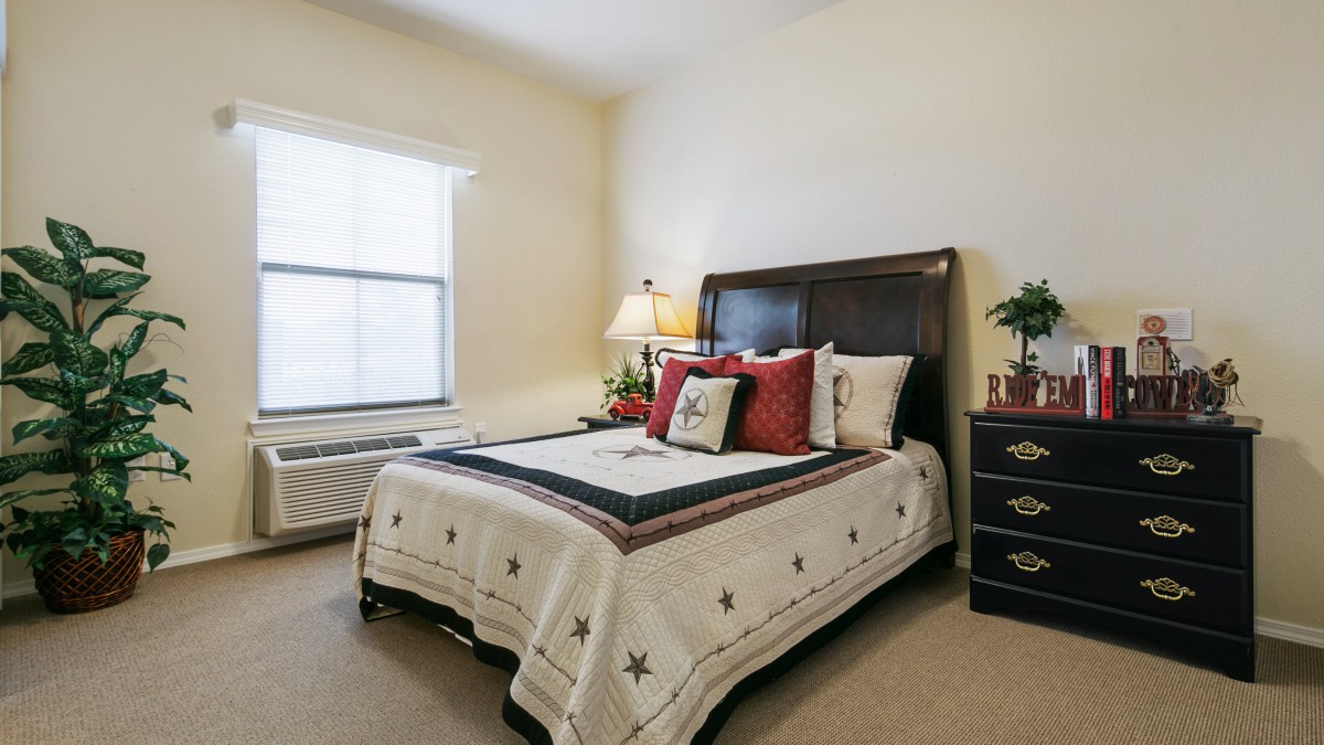A cozy and well-decorated bedroom featuring a bed with patterned bedding, a bedside lamp, and a window allowing natural light in.