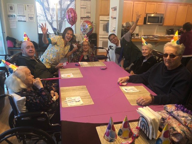 A group of people celebrating a birthday with party hats and balloons around a table.
