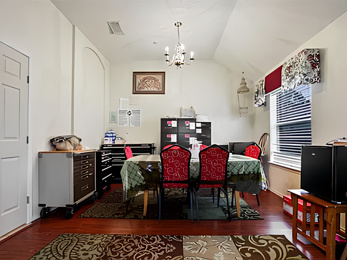 A well-decorated dining room with a table, chairs, and bookshelf, featuring a chandelier and large window for natural light.