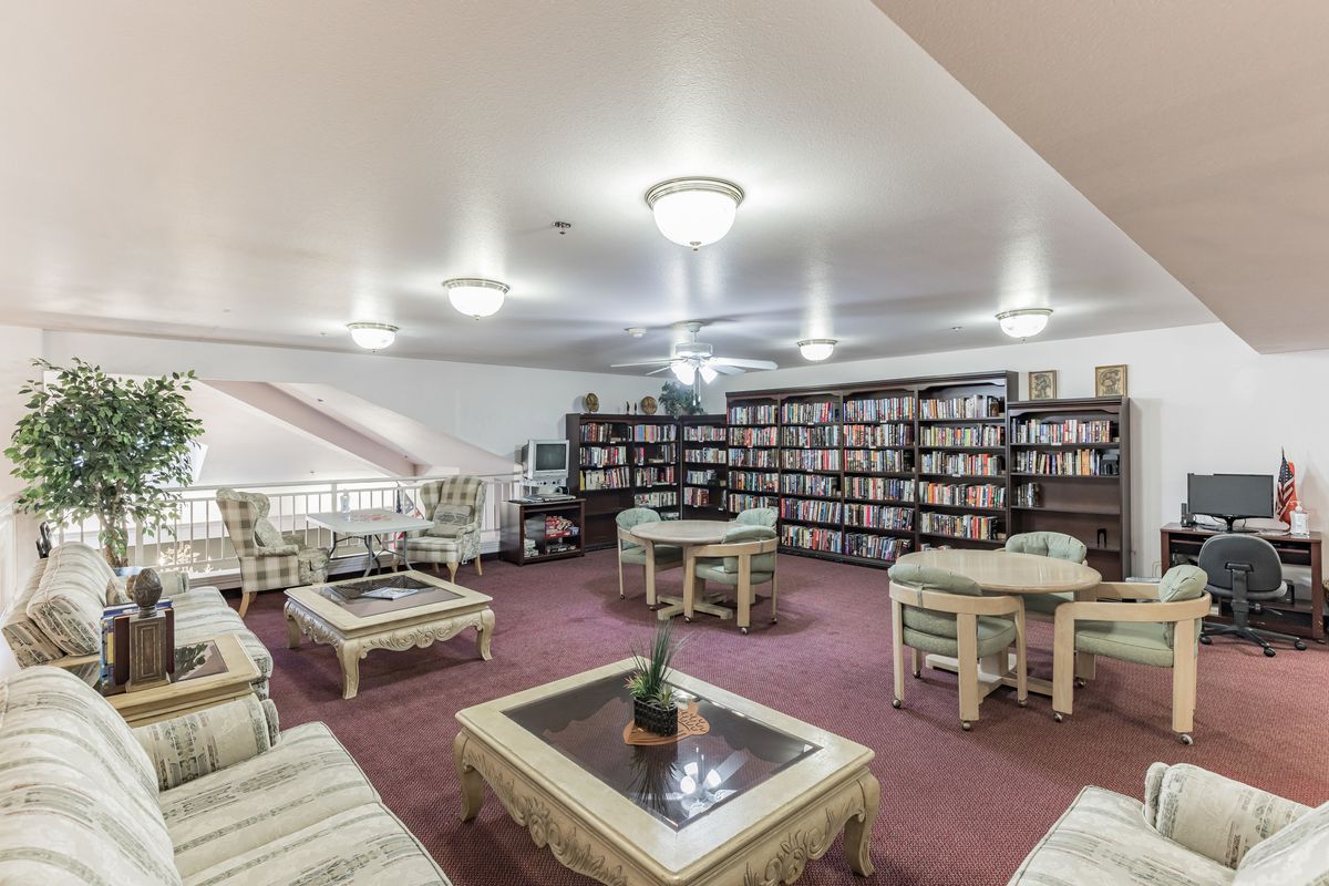 A cozy library featuring bookshelves filled with books, surrounded by comfortable seating and tables on a carpeted floor.