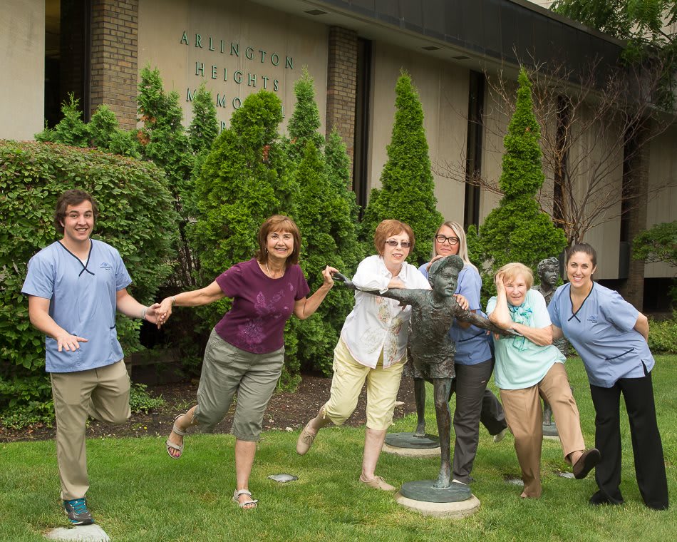 A group of people posing playfully with statues outside a building.