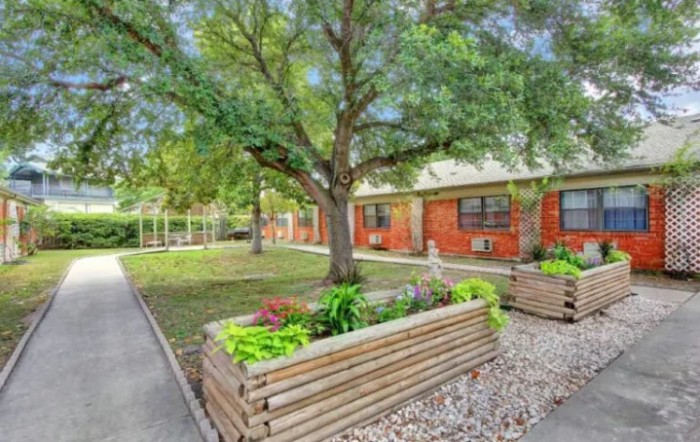 A serene outdoor area featuring planter boxes with lush greenery, set beside a pathway and building.