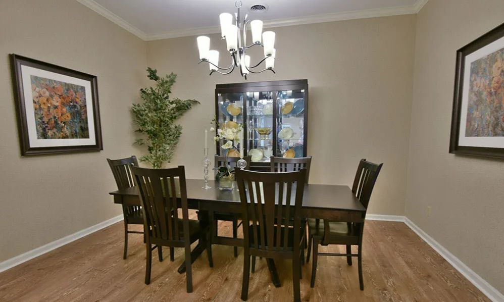 A well-furnished dining room featuring a dark wooden dining table with six chairs, a glass cabinet, and a modern chandelier.
