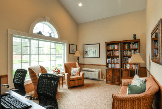 A cozy home office with a large window, bookshelves, and comfortable seating.
