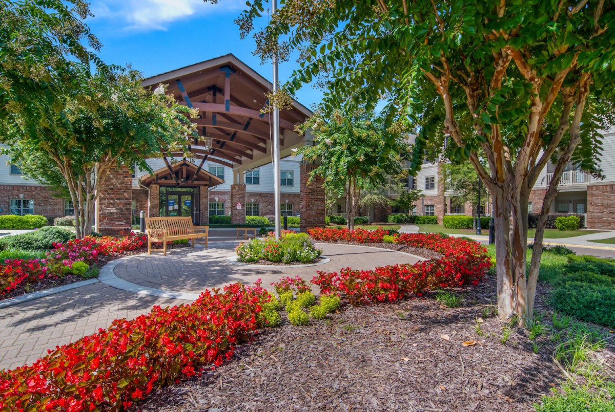 A beautifully landscaped building entrance surrounded by vibrant flowers and lush trees.