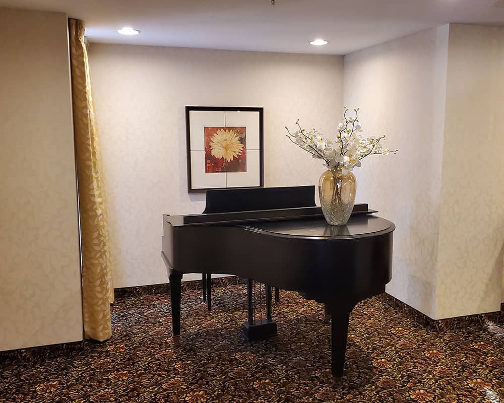 A room with a grand piano, adorned with a vase of flowers, and artwork on the wall.