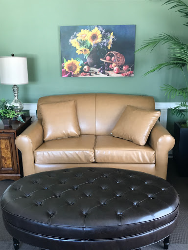 A cozy living room setting featuring a leather couch, an ottoman, and a vibrant piece of artwork.