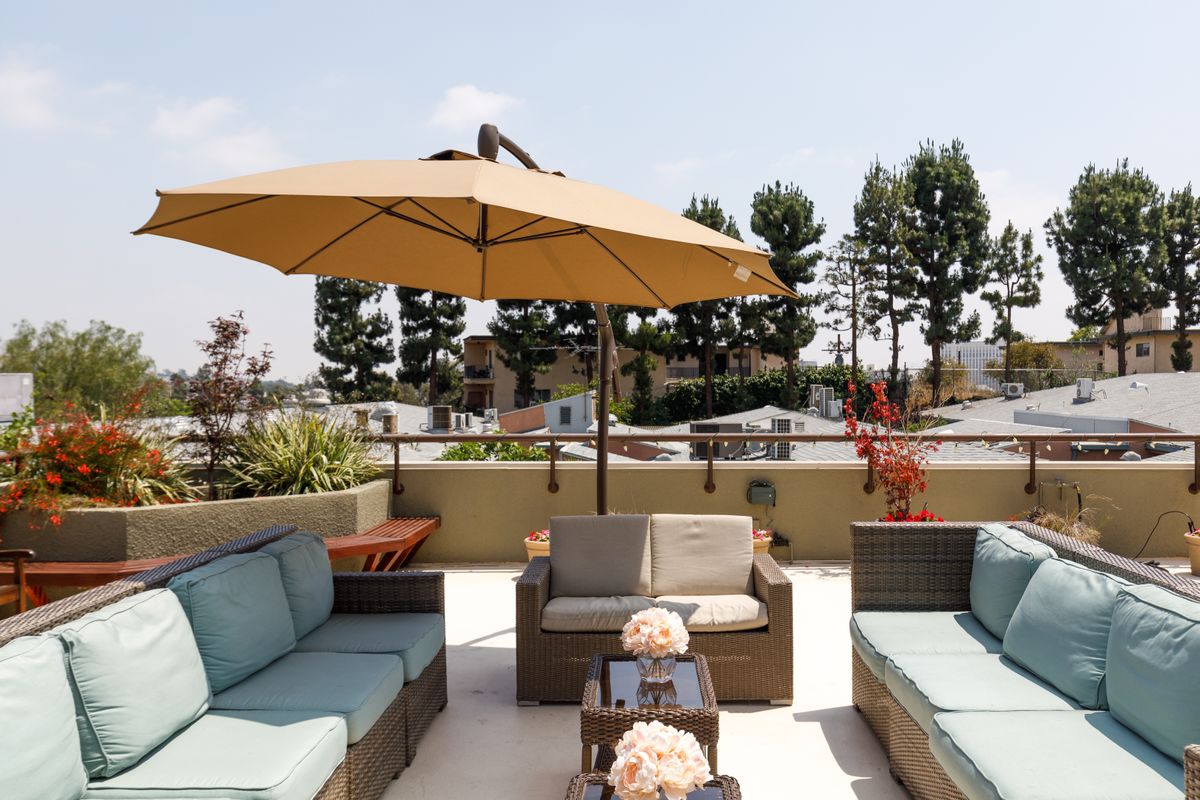 A comfortable outdoor patio with cushioned seating and a large umbrella, surrounded by greenery.
