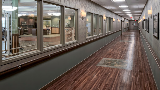 A well-lit hallway featuring wooden flooring and large windows, typical of a commercial or healthcare environment.