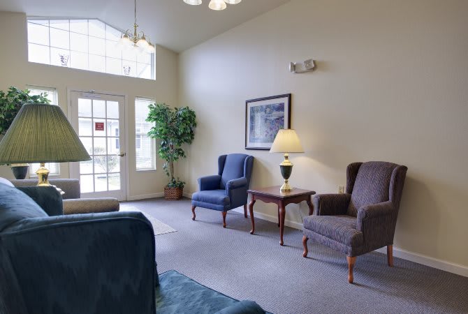 A cozy living room with armchairs, a lamp, and a large window.