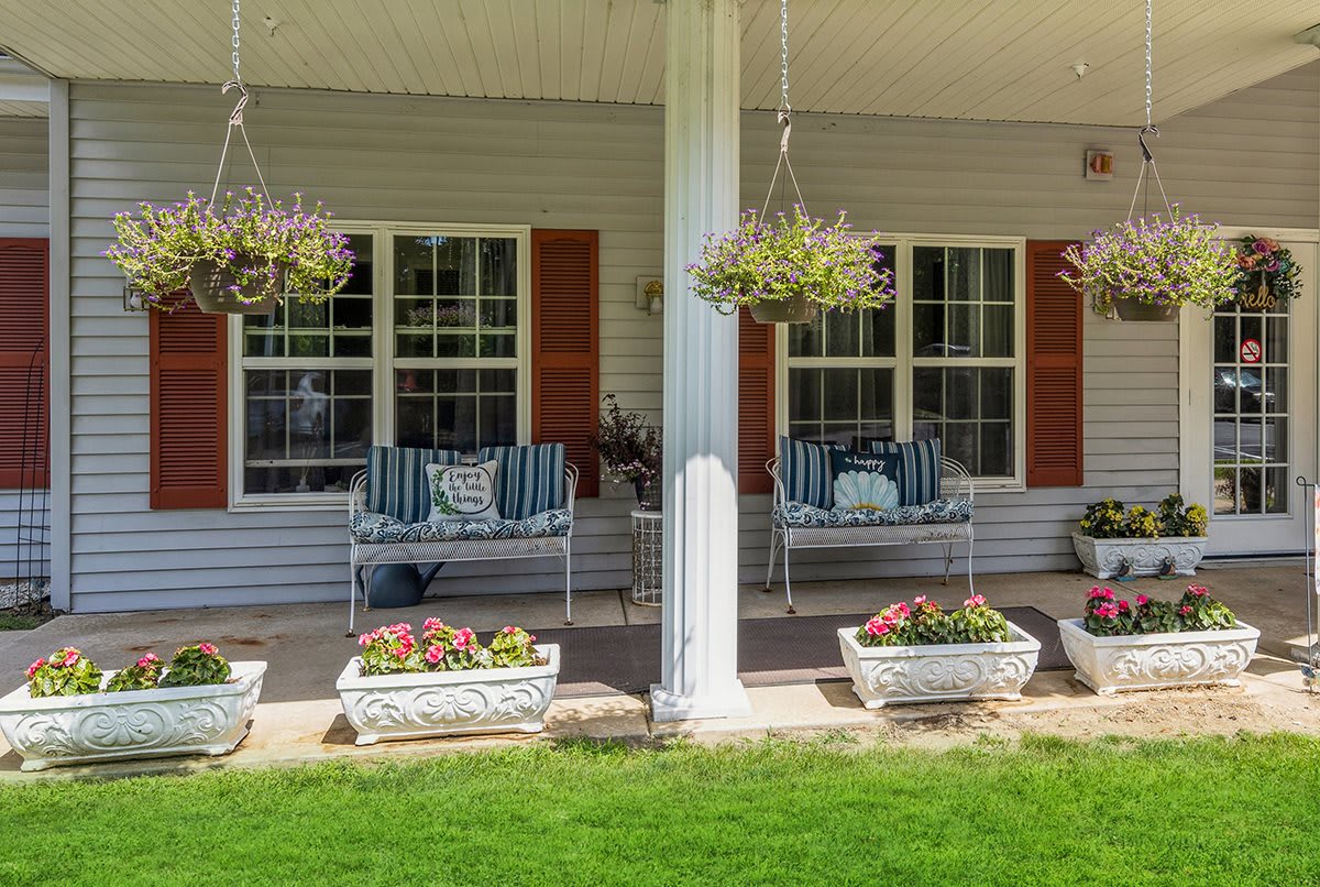 A cozy front porch with seating and vibrant hanging plants.