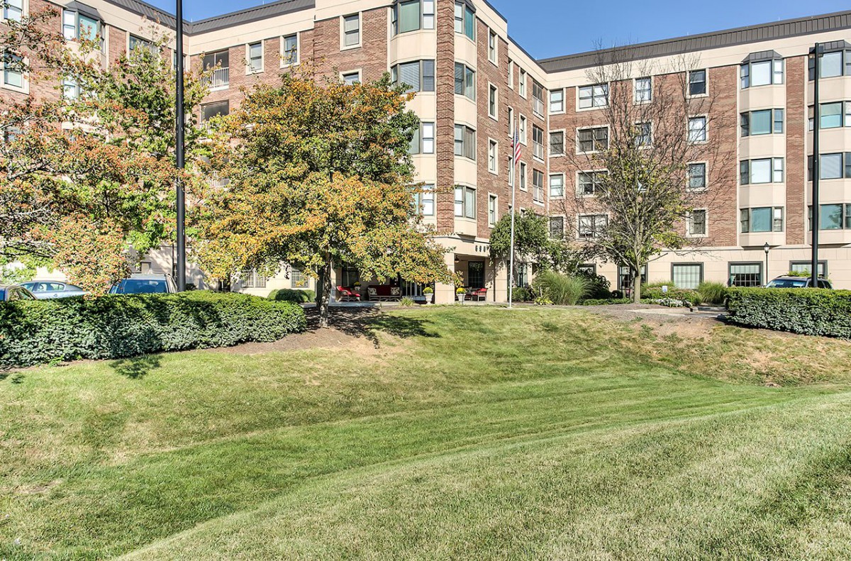 A residential apartment building surrounded by landscaped greenery and trees.