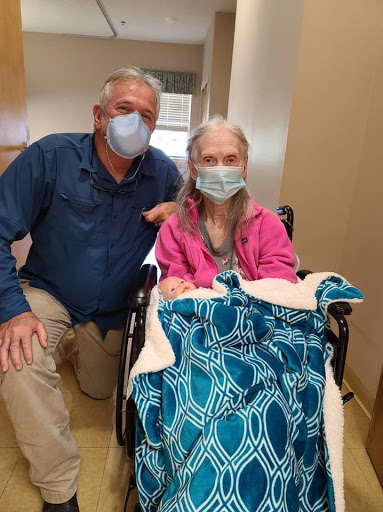 A caregiver and an elderly person pose together in a hospital setting, both wearing masks.