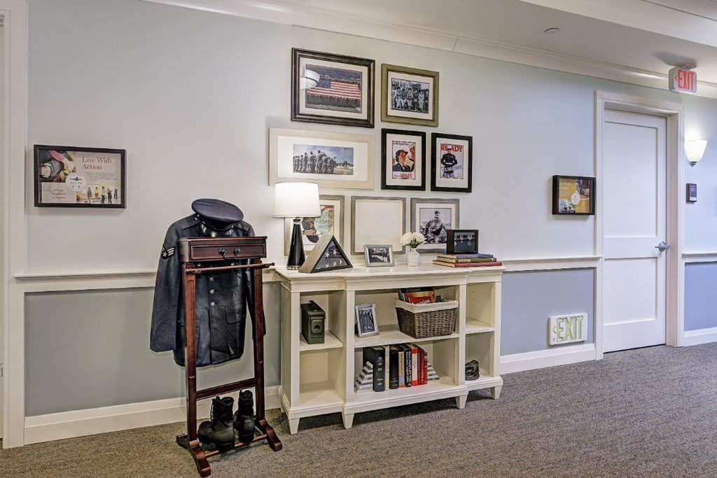A well-decorated interior space showcasing a military uniform on a stand and various framed photographs above a bookshelf.