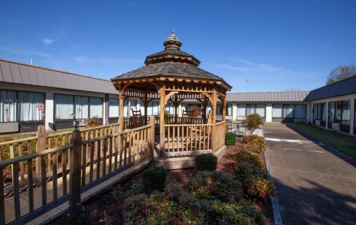 A wooden gazebo situated in a landscaped courtyard surrounded by a building on a clear day.