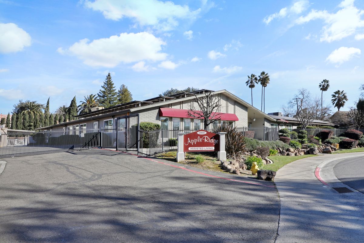 The exterior view of a motel with a driveway and surrounding trees under a blue sky.
