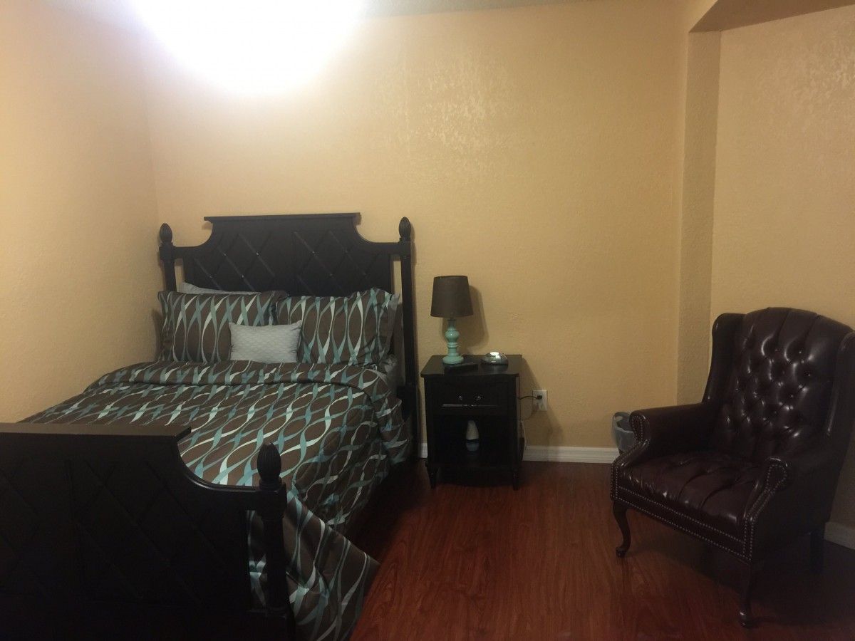 A cozy bedroom with a bed, side table, lamp, and armchair.