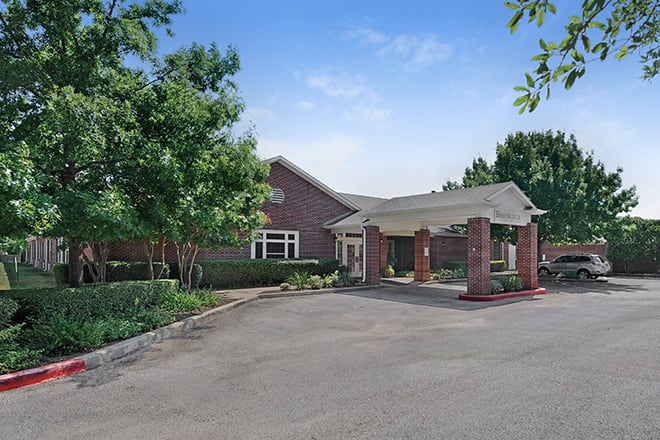 A brick building with a covered entrance and surrounding greenery.