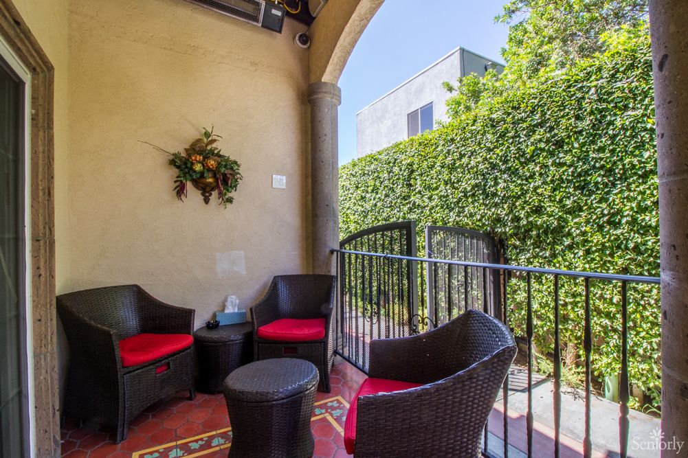 A cozy outdoor patio with wicker chairs and a small table, surrounded by greenery.