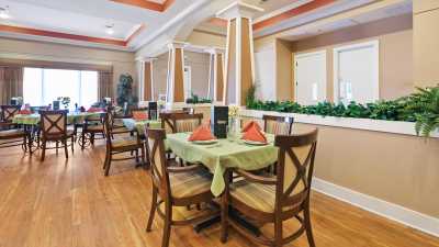 A neatly arranged restaurant dining area with tables and chairs, featuring green tablecloths and orange napkins.