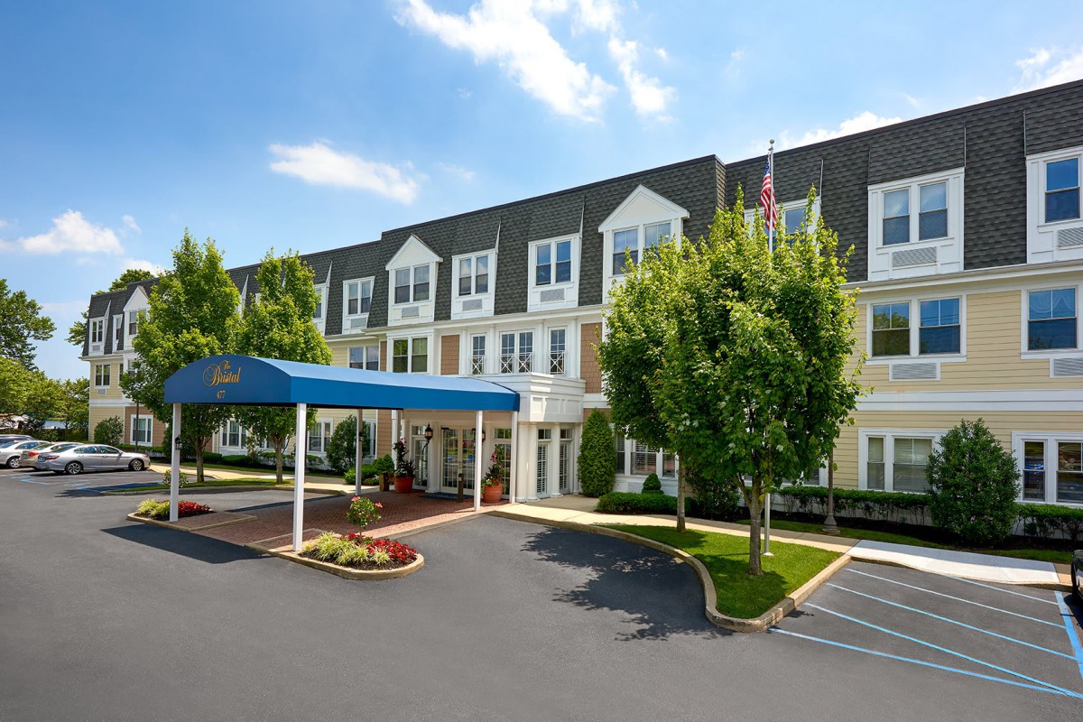 A three-story hotel building with a covered entrance and landscaped surroundings.