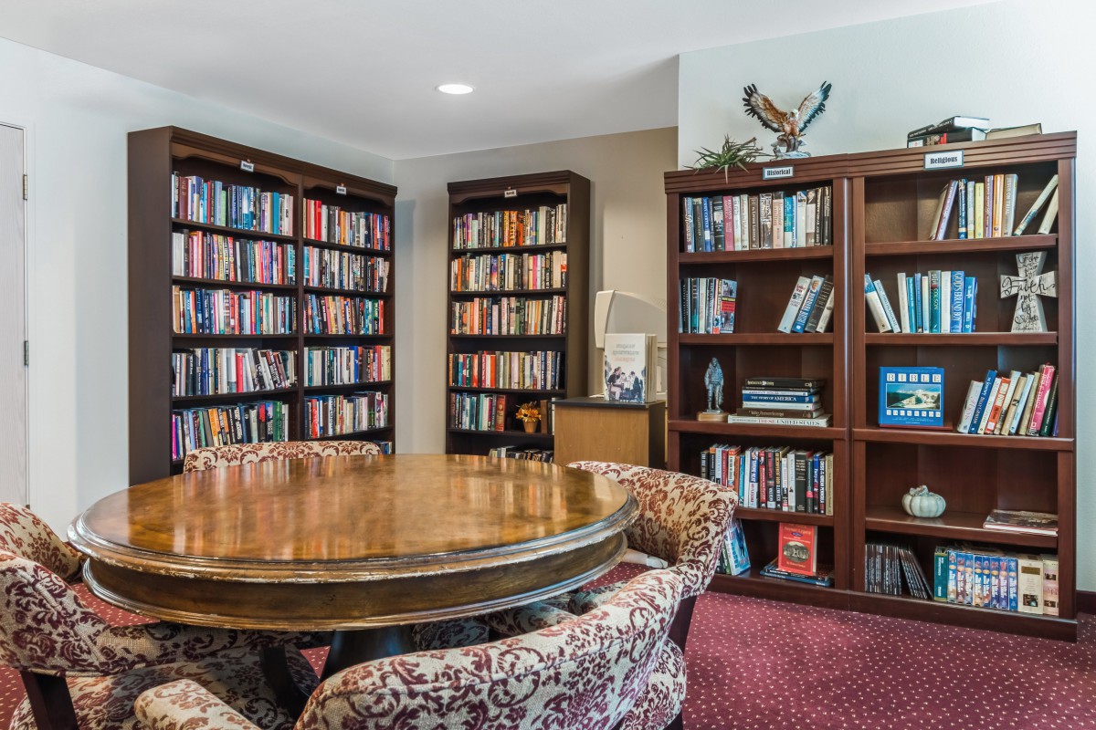 A cozy library room with wooden bookshelves, a round table, and comfortable chairs.
