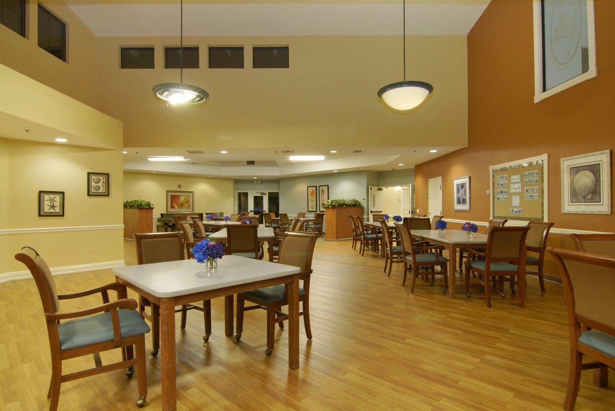 A spacious dining room with multiple tables and chairs, featuring warm lighting and a wooden floor.