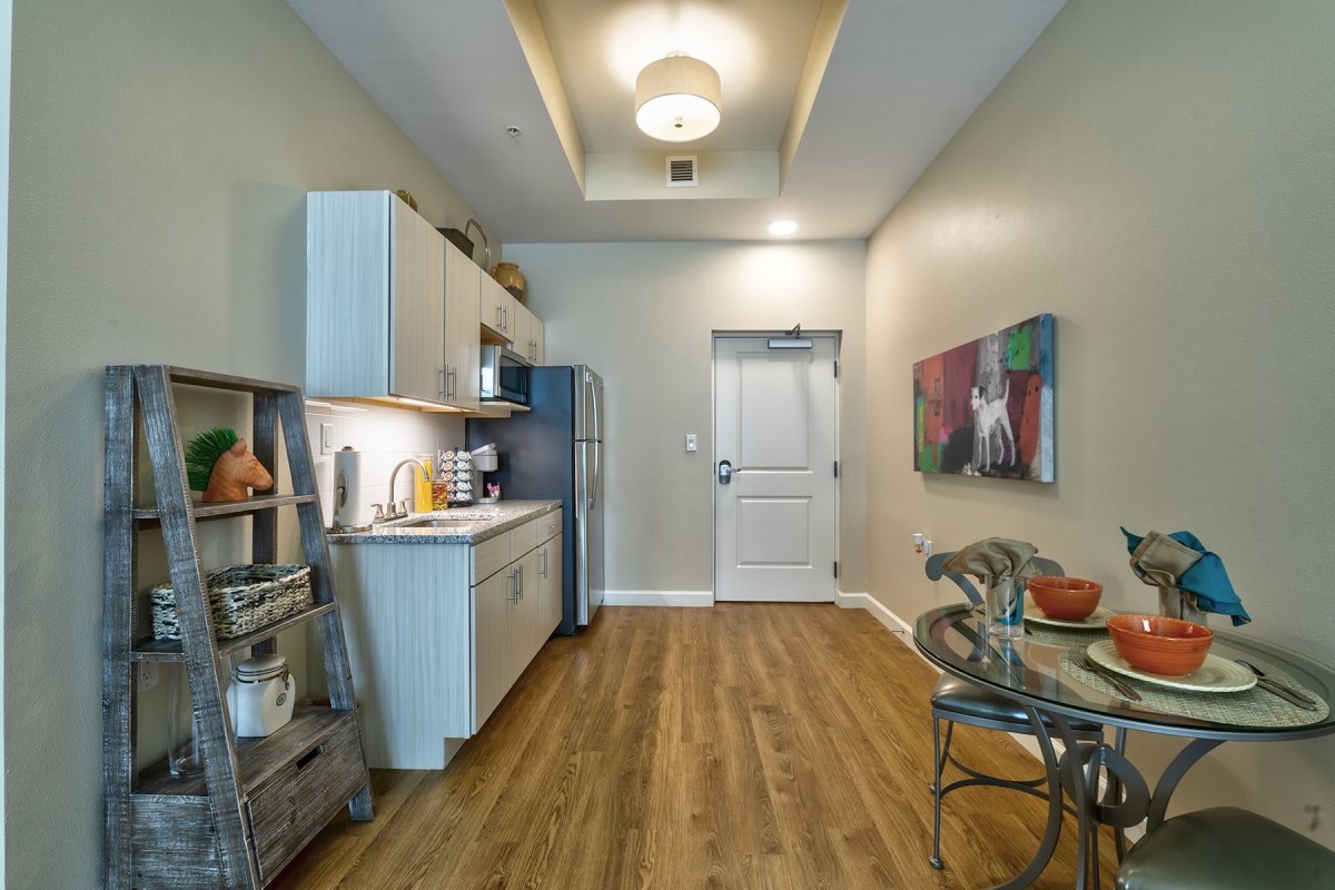 A modern apartment kitchen featuring an open layout with wood flooring and recessed lighting.