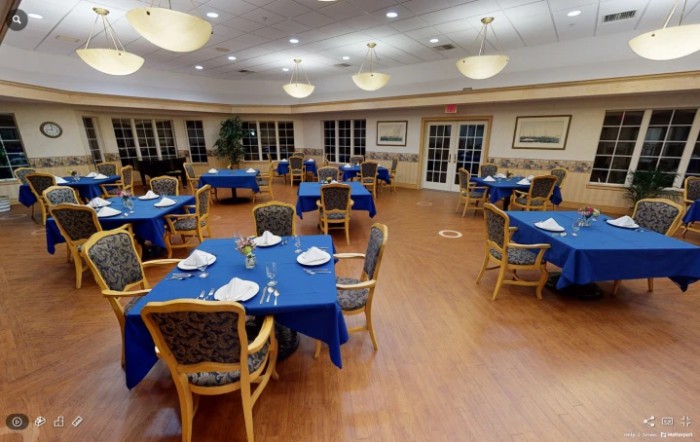 An empty dining room with blue tablecloths and neatly arranged tables and chairs.