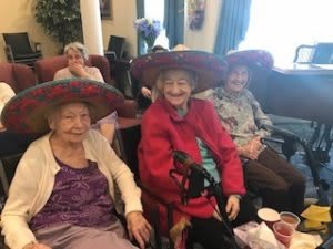 A group of elderly individuals wearing festive hats and smiling indoors.