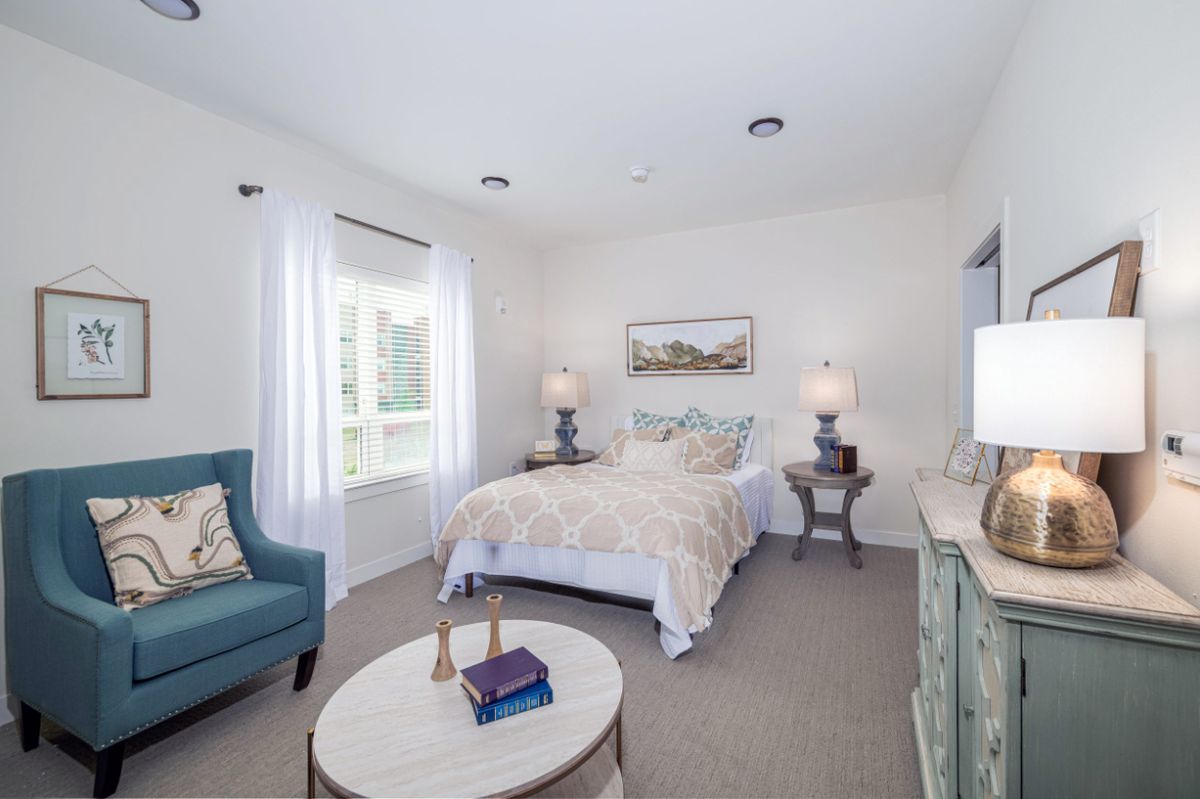 A bright and cozy bedroom with modern decor, featuring a comfortable bed, an armchair, and side tables with lamps.