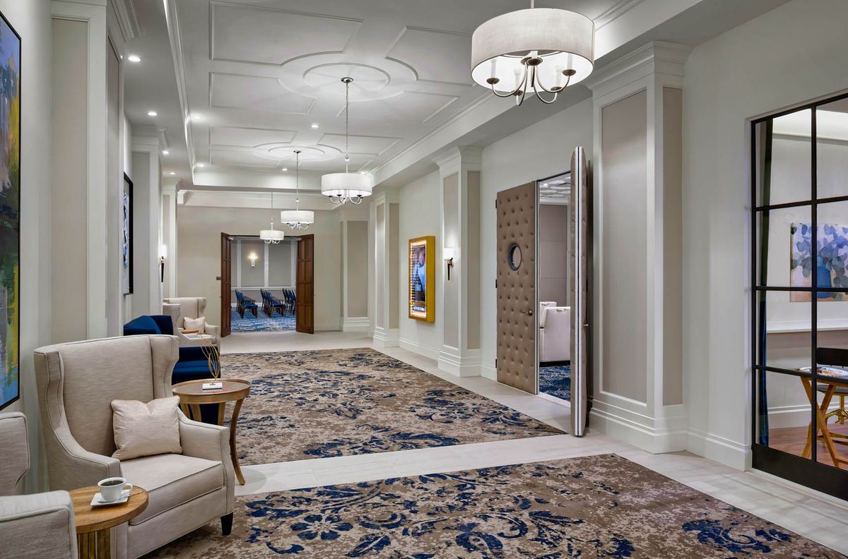 A luxurious hallway with elegant furniture, ornate carpet, and chandeliers.
