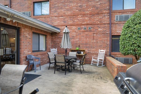 A cozy patio with outdoor furniture, including a table, chairs, and an umbrella against a brick wall.
