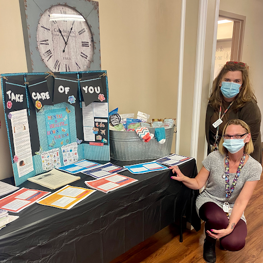 Two women in masks presenting educational materials at an indoor event.