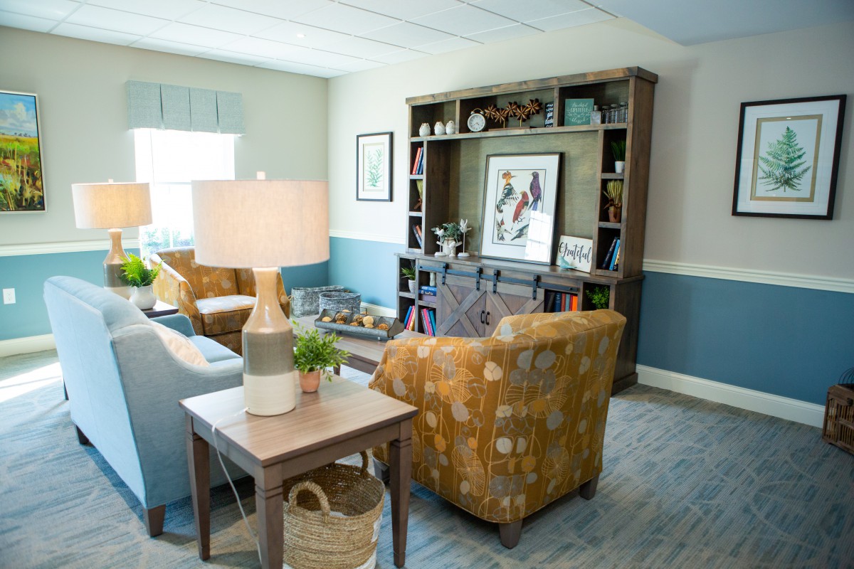 A cozy living room with modern decor, featuring a bookshelf, armchairs, and a table lamp.