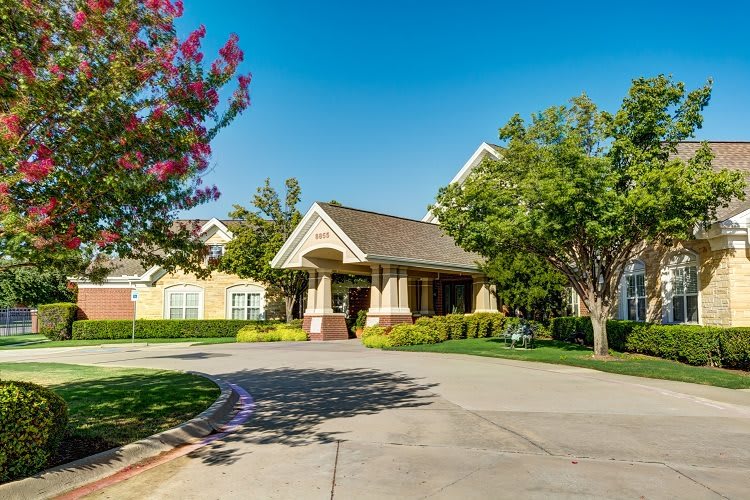 A suburban residential building with a landscaped driveway and trees on a sunny day.