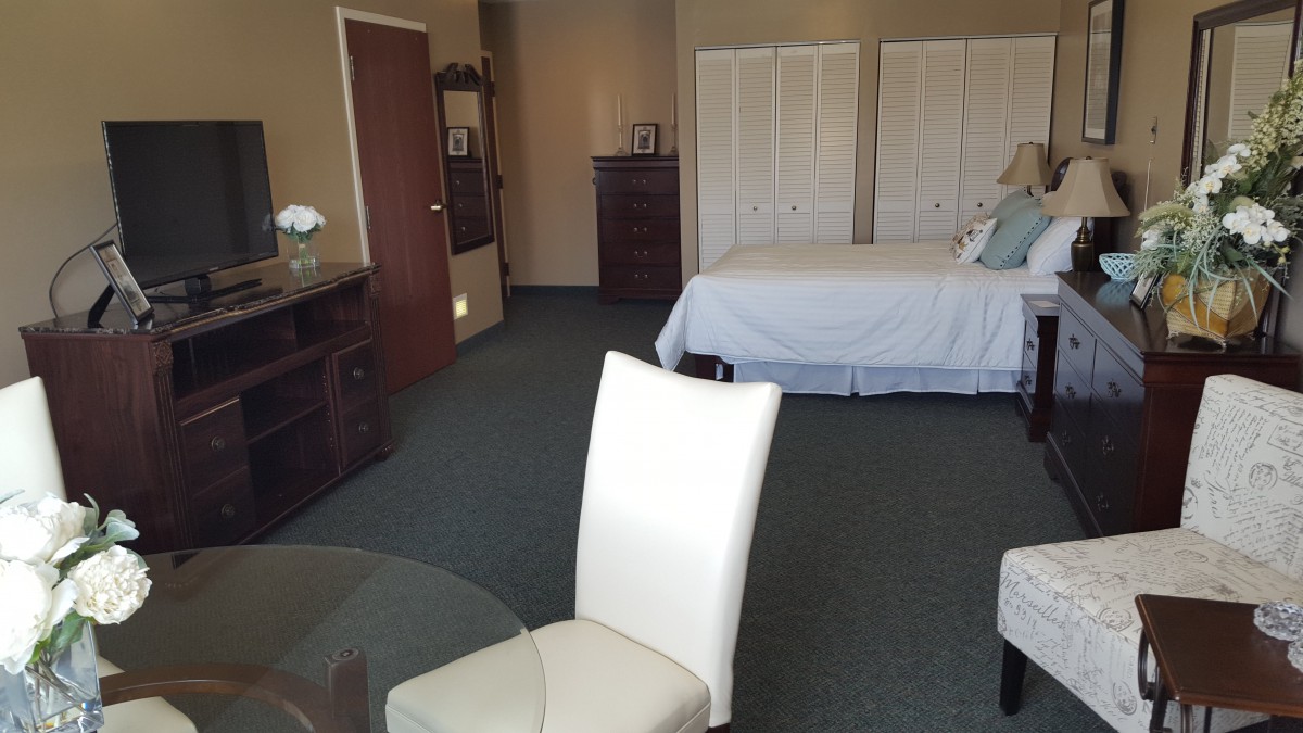 A spacious bedroom with elegant furniture, featuring a bed, chairs, and a dresser.