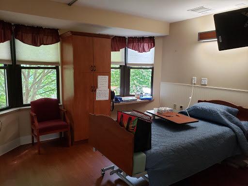 A comfortable hospital room with a patient bed, windows letting in natural light, and seating for visitors.