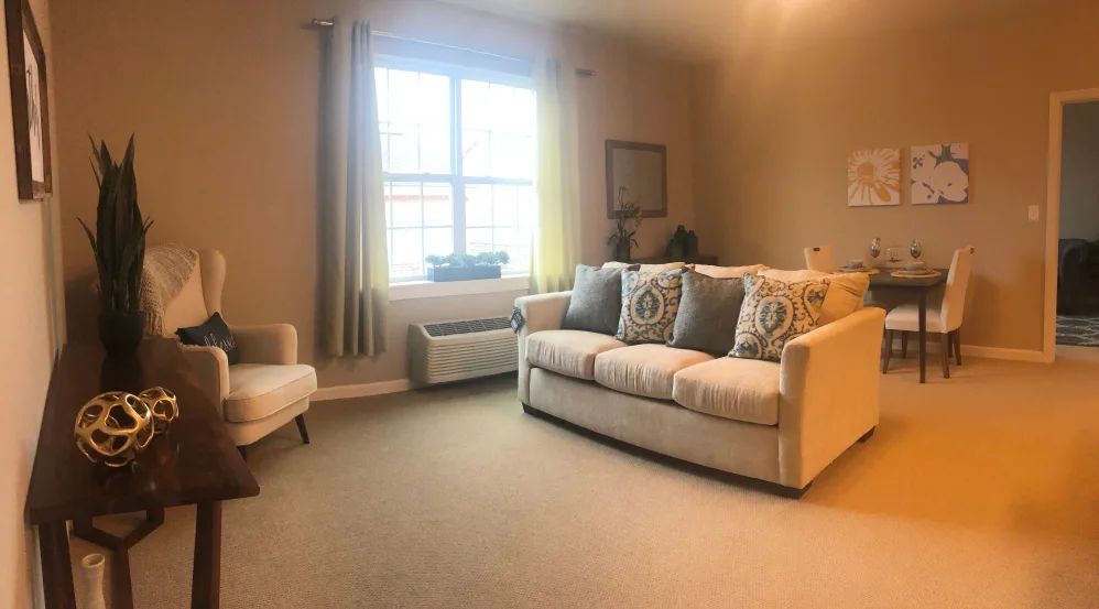 A cozy living room with a beige sofa, decorative cushions, and a large window.